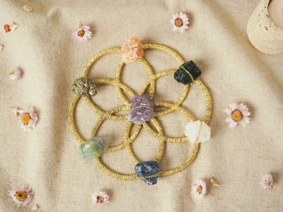 Pierres colorées disposées sur des cercles dorés entrelacés, entourées de petites fleurs sur un tissu beige.